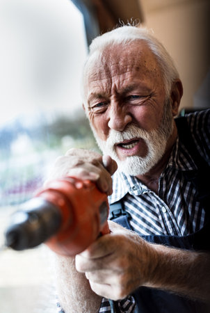 Portrait of senior man working with cordless screwdriver, drilling beside window
