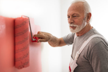Senior man painting white wall with pink color for granddaughter's roomの写真素材