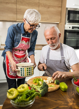 Senior couple preparing soup, husband cutting vegetable while wife holding potの写真素材