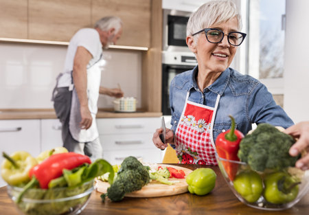 Senior couple preparing soup, wife cutting vegetable while husband cooking in backgroundの写真素材