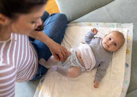 Top view of cute newborn baby lying on back on sofa while mother changing diaperの写真素材