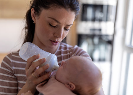 Young mother feeding newborn baby with milk from bottle at homeの写真素材