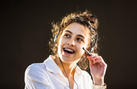 Pretty young woman with headphones and microphone smiling and working on customer service position
