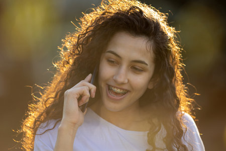 Portrait of cute teenage girl talking on mobile phone outdoor in nature at sunset in spring or summer timeの写真素材