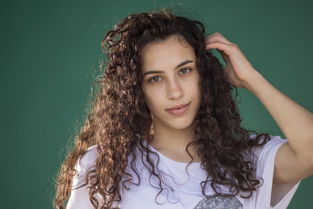 Portrait of pretty teenage girl with curly hair isolated against green backgroundの写真素材
