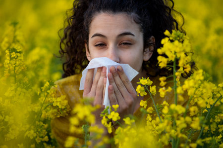 Pretty young woman sneezing and blowing nose in yellow ripe rapeseed in early summer. Allergy reaction conceptの写真素材