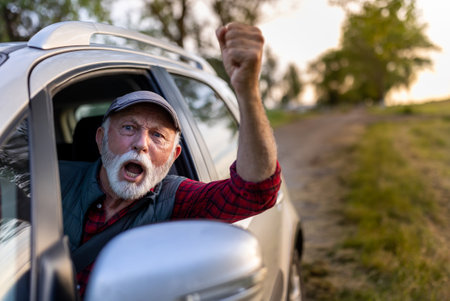 Senior man driving car, looking through window and arguing with somebodyの写真素材