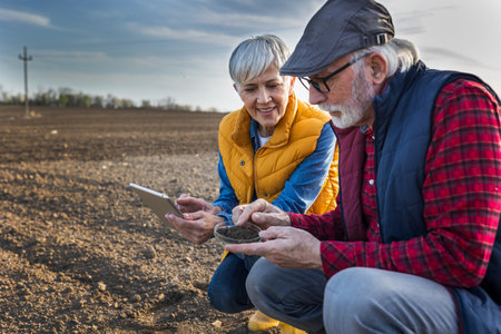 Senior farmer man and woman checking dirt quality in petri dish in agricultural field in spring timeの写真素材