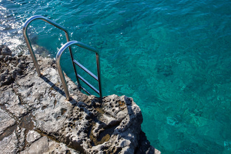 Stainless steel ladder on rock on sea coast. Blue transparent water in natural poolの写真素材