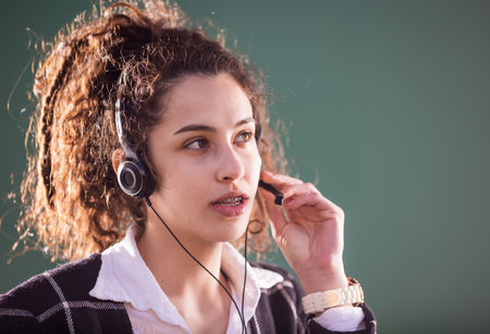 Pretty young woman with headphones and microphone smiling and working on customer service positionの写真素材