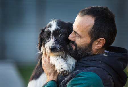 Lovely moment when mature man holding and hugging cute dog in shelter. Love, care and tendernessの写真素材