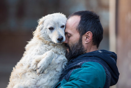 Lovely moment when mature man holding and hugging cute abandoned dog in shelter. Love, care and tendernessの写真素材
