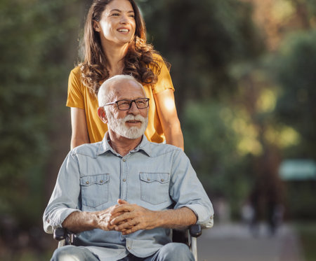 Young woman caregiver pushing senior man in wheelchair in parkの写真素材