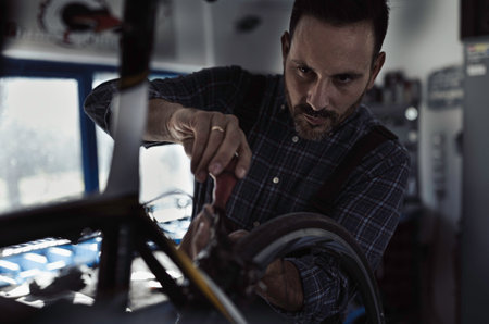 Handsome repairman in overalls working on bicycle in workshop