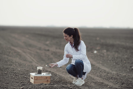 Pretty young agronomist in white coat checking soil condition before sowing in early springの写真素材