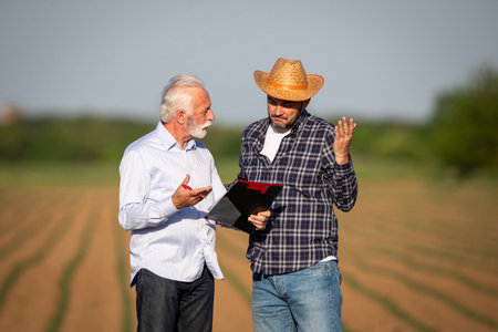 Senior business man talking to mature adult farmer about business in agricultural field in spring timeの写真素材
