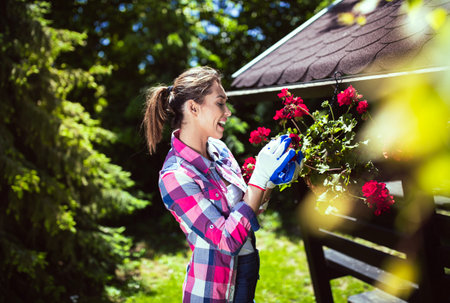 Woman in checked shirt smiling as she tends to colorful flowers in a garden. Lush greenery surrounds her, creating a serene outdoor atmosphereの写真素材