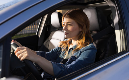 Woman with red hair smiling as she driving car. The interior is modern and well-lit during daytime