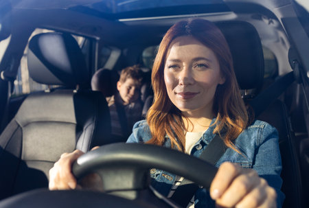 Woman smiling while driving car, with child seated comfortably in backseat. The sunlight brightens...