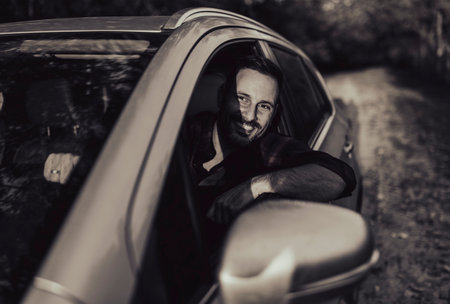 Man driving car, smiling while gripping the steering wheel and looking through side window. Bright...