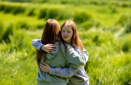 Redhead twin sisters lovingly hugging each other in the grasslands, openly showing affection and a...