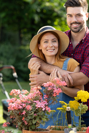 Cheerful couple embraces while surrounded by colorful flowers in sunny garden. They are engaged in...