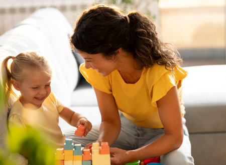 Mother and child enjoy joyful afternoon playing with colorful building blocks in sunlit room,...