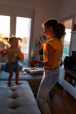 Mother and her young daughter share joyful moment in their living room, dancing in the warm glow of...