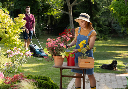 Happy family working hard in their backyard on a sunny afternoon. Pretty wife repotting flowers...