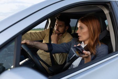Couple in car debating directions, man pointing at road while woman drives with one hand holding...