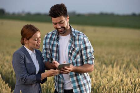 Farmer and woman in formal attire discussing business while looking at tablet in wheat field