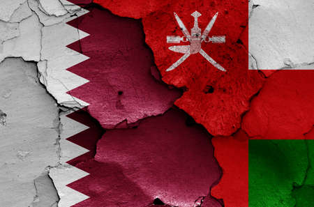 flags of Qatar and Oman painted on cracked wallの写真素材