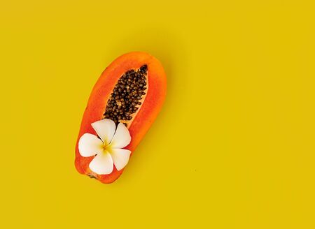 Half fresh ripe papaya and tropical flower on a yellow background. Space for textの写真素材