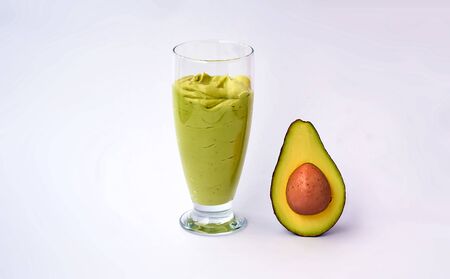 A glass of avocado and spinach smoothies and half an avocado on white background. Fitness product. Dietary sports nutrition.の写真素材