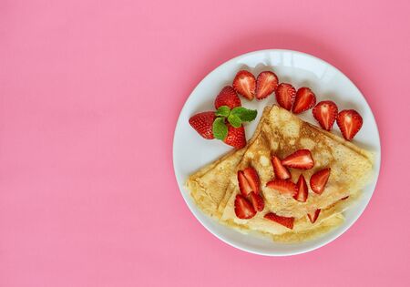 Sliced strawberries with homemade pancakes for breakfast. White plate on a pink background. Free...