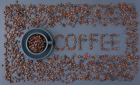 Top view of Coffee word made from coffee beans by cup of coffee beans on gray textured backgroundの写真素材