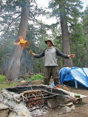 A hiker holding a burning branch above an outdoor fire place in the Sierra Neavada Mountains.の写真素材
