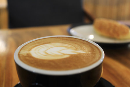 A glass of coffee latte with floral motifs on the coffee surface is on the tableの写真素材