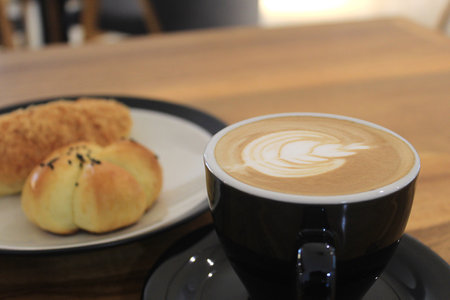 A glass of coffee latte with floral motifs on the coffee surface is on the tableの写真素材