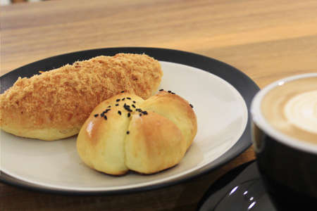 A glass of coffee latte with floral motifs on the coffee surface side by side with pastries on the tableの写真素材
