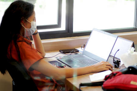 Coronavirus (COVID-19) concept. Asian woman wearing face mask working on laptop computer at home.
