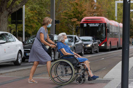 Zaragoza, Spain - August 18, 2020: Elderly woman in wheelchair wears face mask, due to the coronavirus pandemic, in the central area of Zaragoza.のeditorial素材