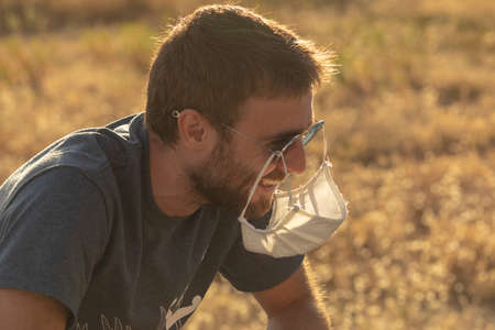 A young man laughs foolishly, as he hangs his protective face mask from his sunglasses.