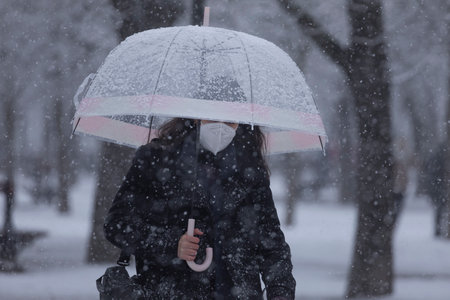 Photo for Madrid, Spain - January 07, 2021: A young girl walks fast in the middle of the blizzard, through the Buen Retiro park in Madrid, in the middle of a snowy day, due to a wave of polar cold. - Royalty Free Image