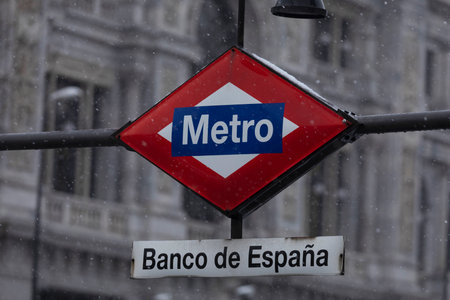 Madrid, Spain - January 08, 2021: Metro Madrid sign, frozen, covered with ice and snow, in the middle of a freezing blizzard, due to the Filomena polar cold front, in Madrid, Bank of Spain area.のeditorial素材