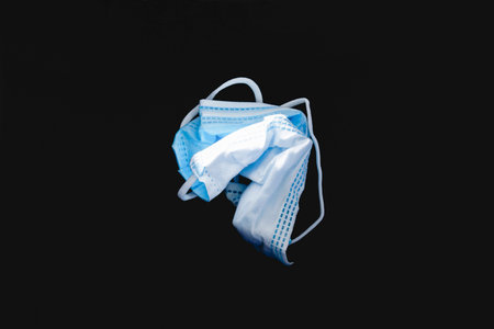 Protective face mask made of blue plastic, on a dark background, wrinkled, dirty and discarded,...