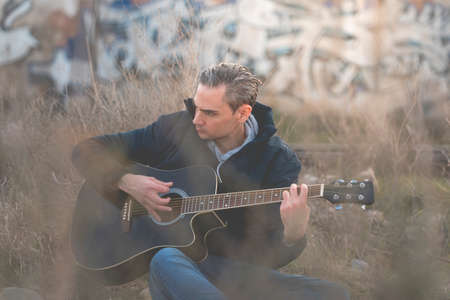 A young white man, with gray hair, musician and artist, plays an elegant black guitar, and composes...
