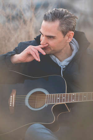 A young white man, with gray hair, musician and artist, plays an elegant black guitar, and composes...