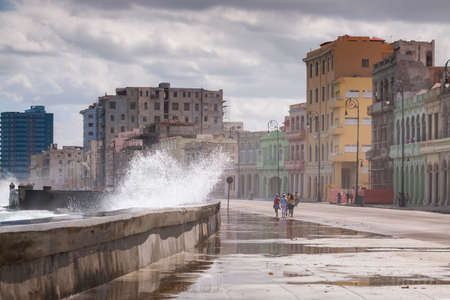 Havana, Cuba - March 23, 2010: A strong wave jumps over the wall that protects the Malecon promenade, in the center of Havana, leaving the entire sidewalk wet and full of algae on a windy day.のeditorial素材