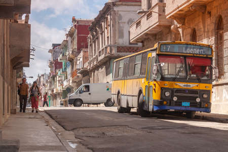 Havana, Cuba - March 23, 2010: A western tourist couple walk down a typical street in the central area of Havana, not far from the Malecon, where an old yellow bus is parked.のeditorial素材